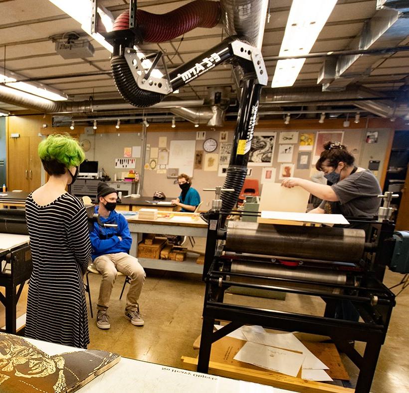 Professor and students learning printmaking on the press